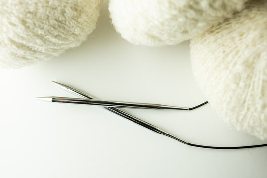 Knitting needles with while boucle yarn on a white background