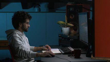 Young adult office worker sitting at desk in modern workspace late at night / active student working at computer at evening in dark room, blue background moonlight.