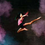 Fototapeta Sport - Street dance girl dancer jumping up dancing in neon light doing gymnastic exercises in studio on dark wall
