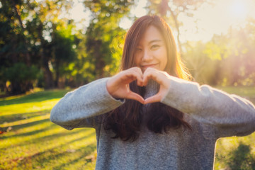 A beautiful asian woman making heart hand sign in the park before sunset