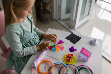 Cute little girl makes a plastic house, draws parts with a 3D pen. STEM and STEAM education. Development, modeling, education, design with hot plastic. Modern technologies. DIY.