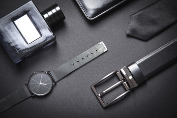 Tie, belt, wristwatch and perfume on the black background. Men accessories