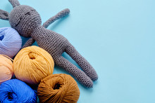 Top View Of The Bright Color Yarn Clews With Grey Stuffed Amigurumi Bunny On The Blue Background. Concept Of Amigurumi Toy Making, Handcrafting, Knitting, Hobbie