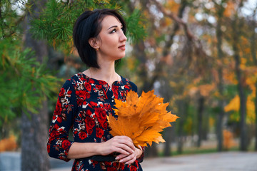 Wall Mural - Beautiful elegant woman standing and posing with bouquet of yellow leaves in autumn city park