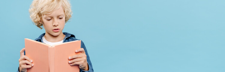 panoramic shot of blonde and cute kid reading book isolated on blue