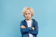 © LIGHTFIELD STUDIOS - sad and cute kid with crossed arms looking at camera isolated on blue