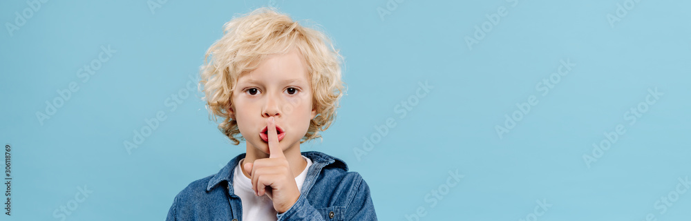 panoramic shot of cute kid showing secret gesture and looking at camera isolated on blue - obrazy, fototapety, plakaty 