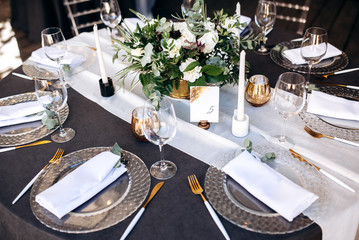 Festive round table which is beautifully decorated with plates, candles and a beautiful composition of flowers and table number in the center