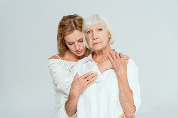 attractive mother and daughter hugging and looking at camera isolated on grey