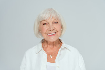 attractive and smiling woman looking at camera isolated on grey