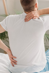 Wall Mural - back view of man sitting on bed and suffering from back pain