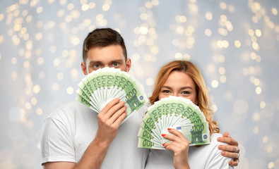 Poster - finance, saving and people concept - portrait of happy couple in white t-shirts with euro money over festive lights background