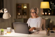 © Syda Productions - technology, old age and people concept - senior woman in glasses with laptop working at home in evening
