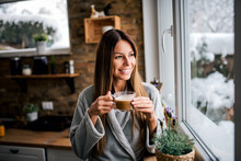 Beautiful Smiling Brunette Looking Through Window And Drinking Coffee In The Kitchen.