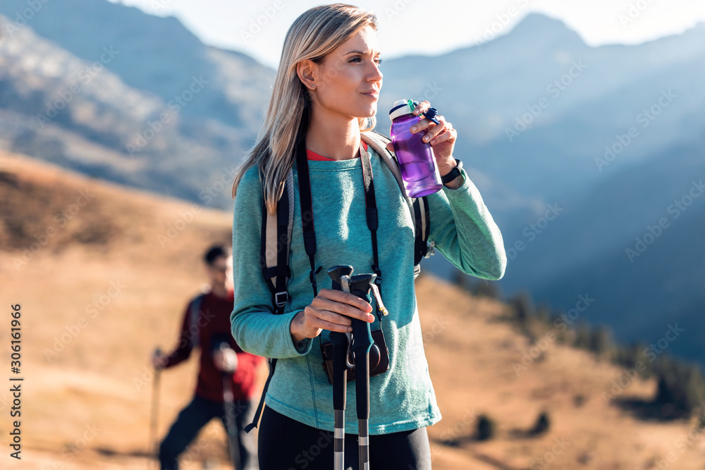 Pretty young woman traveler with backpack looking to the side while drinking water on mountain. - obrazy, fototapety, plakaty 
