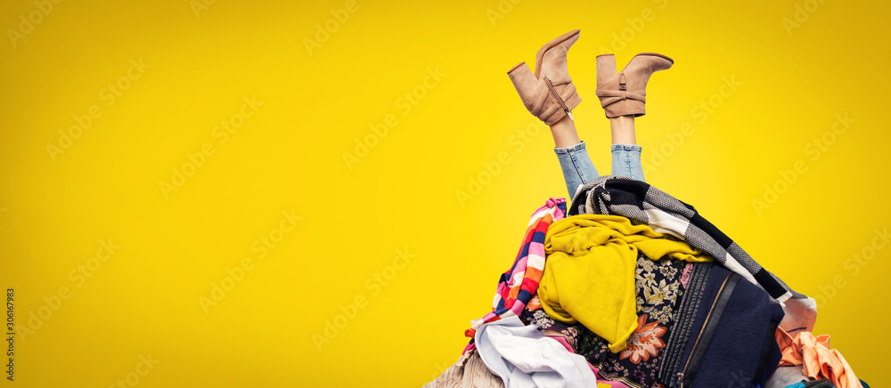 woman legs out of clothes pile on yellow background with copy space - obrazy, fototapety, plakaty 