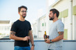 © Mangostar - Two male friends drinking beer and talking on outdoor terrace. Two young men in casual meeting outside. Friendship or hangout concept