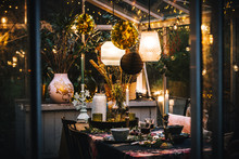 Decorated Greenhouse In Trendy Christmas Setting With Dinner Table, Candles And Christmas Lights.