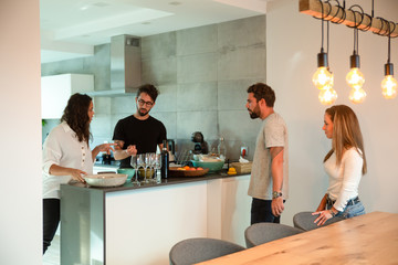 two couples gathering together in kitchen to have dinner and drink wine. young men and women in casu