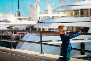 cute boy looking at luxury yachts on the quay