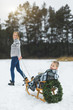 © sofiko14 - Winter family fun holidays. Happy mom in knitted sweater and jeans carries her little son on a wooden sled decorated with Christmas wreath in a winter snowy forest. Merry christmas and happy new year