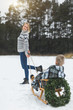 © sofiko14 - Pretty young mother pulling decorated wooden sled with her son sitting on it in winter snowy day at nature.