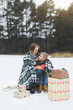 © sofiko14 - Mother and baby sitting on wooden sledge in winter forest and drinking hot tea. Christmas gifts presents on the snow. Winter snowy forest on the background. Christmas vacation.