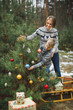 © sofiko14 - Merry Christmas and Happy Holidays. Mom and son decorate the Xmas tree outdoors. Wooden sledge and presents, Christmas wreath