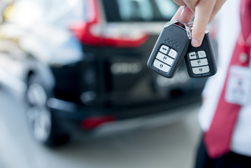 Wall Mural - Close-up of a car key - a young man holding a new car key in the car showroom, new key design concept or background blur material