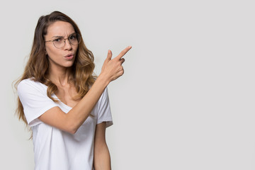 Wall Mural - Doubting young woman wearing glasses pointing finger at copy space