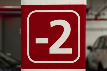 -2 floor sign carpark in parking garage Red brown burgundy in colour underground multi story building dry safe. Health and safety symbols painted on white column cars parked in the background