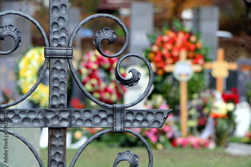 Fotomural Am Friedhof, Im Vordergrund ein schmiedeeisernes Grabkreuz, im unscharfen Hinter