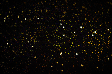 Beautiful Christmas light background. Abstract glitter bokeh and scattered sparkles in gold, on black