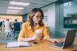 © BullRun - Beautiful woman in classic glasses searching information on college informative website connected to 4g wireless in public coffee shop, Chinese female freelancer typing content text via netbook