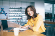 © BullRun - Portrait of positive hipster student sitting at desktop with knowledge textbook and laptop for e learning and smiling at camera, successful female freelancer working remotely with distance plan