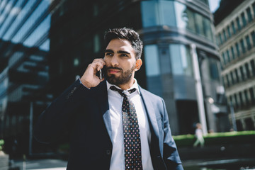 Spanish bearded man using roaming connection for making international conversation with boss during business travel, serious male entrepreneur calling to operator via application on smartphone