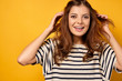 © bestsenny - A brunette in a striped T-shirt stands on a yellow background, joyfully looks into the camera, throwing hair away from the face