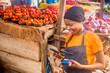 © Confidence - young african woman selling in a local african market holding a mobile point of sale system and using her mobile phone