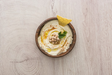 Poster - top view of delicious hummus with chickpeas and nacho in bowl on beige wooden table