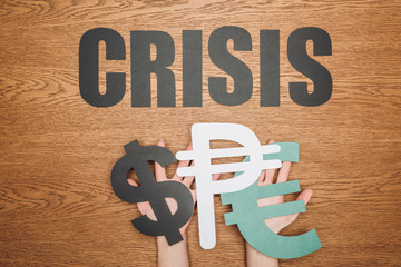 Poster - cropped view of woman holding dollar, peso and euro paper cut symbols, and word crisis on wooden desk