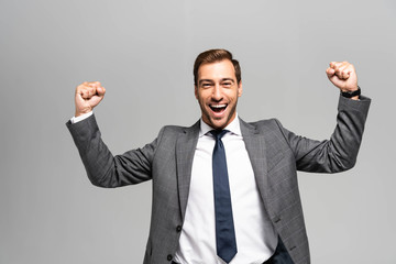 handsome and smiling businessman in suit showing yes gesture isolated on grey