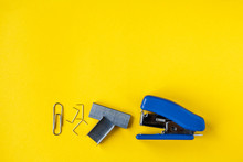 Blue stapler with metal staples and paper clip on yellow background. Top view. Copy, empty space for text. Minimalistic concept