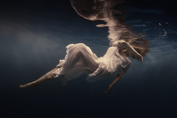 Woman in a beautiful dress swims underwater