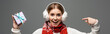 panoramic shot of excited girl in scarf and ear warmers pointing at christmas gift, isolated on grey