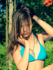 Wall Mural - Beautiful little girl in a blue bathing suit among exotic greenery on a warm summer day. Beautiful portrait of a beautiful girl.