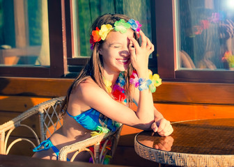 Wall Mural - Girl in a swimsuit on the beach near the bungalow. Attractive young girl Sitting on the chair at a table in a bungalow