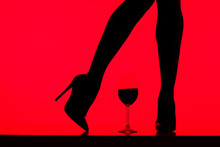 Cropped View Of Black Silhouette Of Girl In Heels With Glass Of Wine Isolated On Red