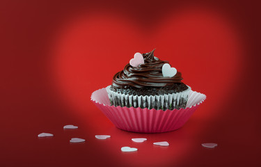 Chocolate cupcake with pink eatable hearts on red background