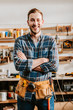 © LIGHTFIELD STUDIOS - happy carpenter in apron standing with crossed arms