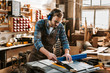 © LIGHTFIELD STUDIOS - handsome woodworker in protective headphones and apron holding plank near circular saw